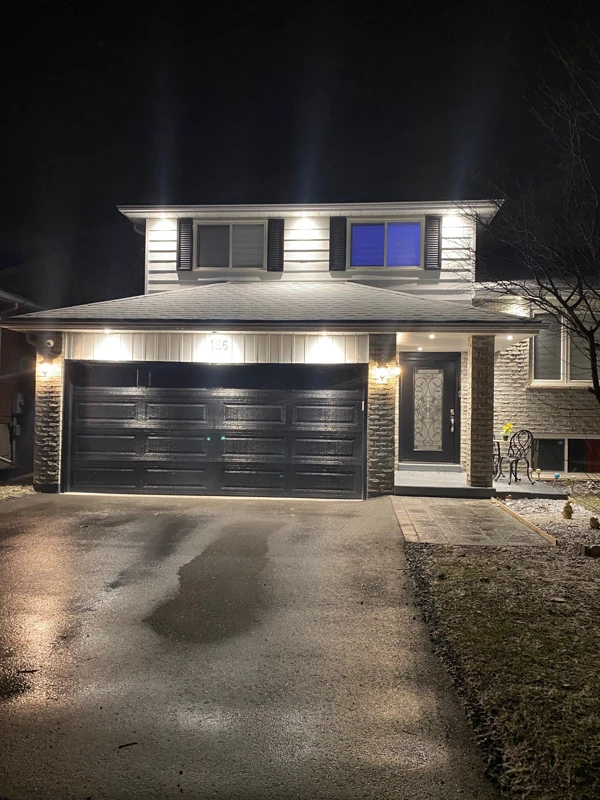 Exterior pot lights accent the rooflines and garage of a two-storey home at night